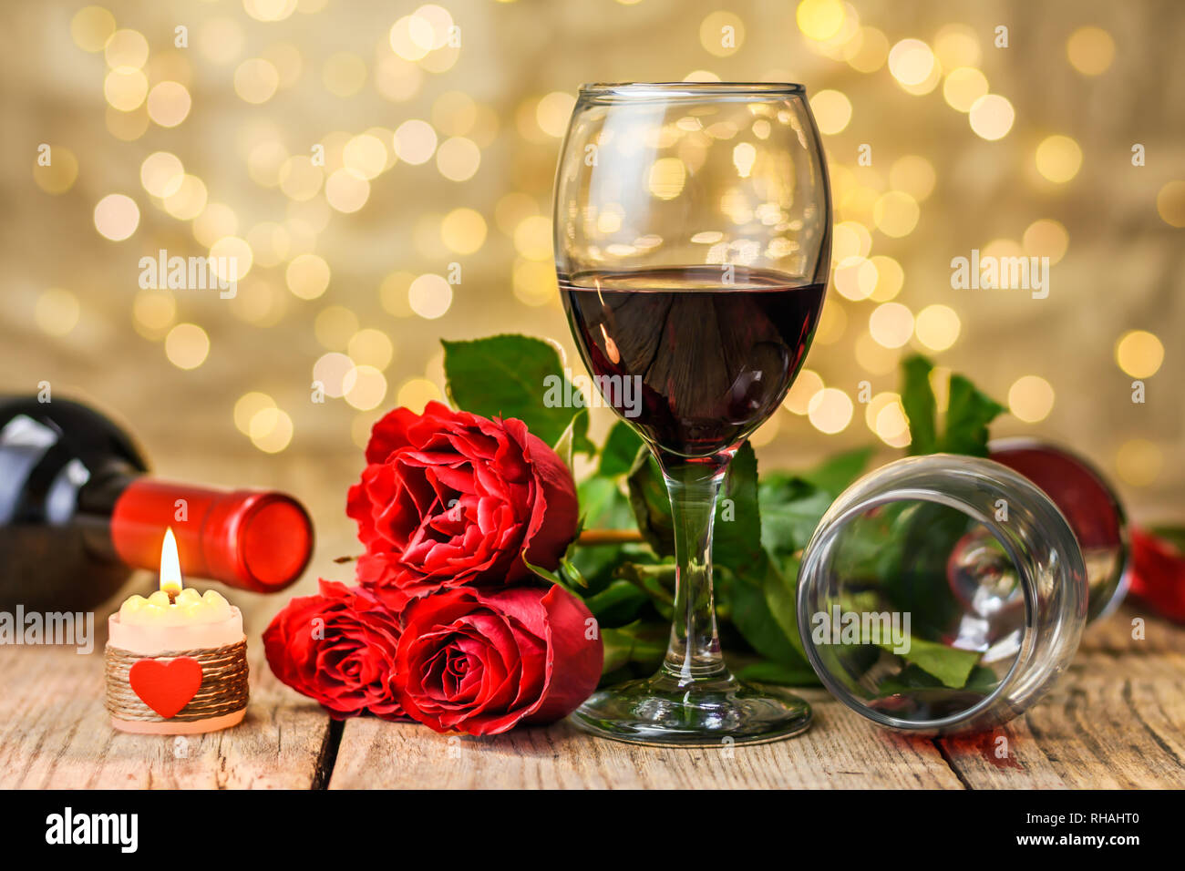Il giorno di San Valentino del concetto. Due bicchieri di vino, rose rosse, bottiglia di vino e la masterizzazione di candela su una tavola in legno rustico. Foto Stock