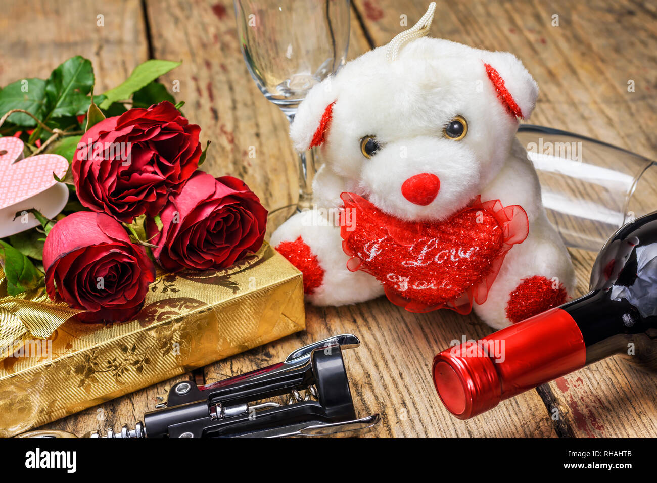 Il giorno di San Valentino del concetto. White il giocattolo di peluche orso, bottiglia per vino, rose rosse, confezione regalo, cavatappi e bicchieri di vino sulla lavagna in legno. Foto Stock