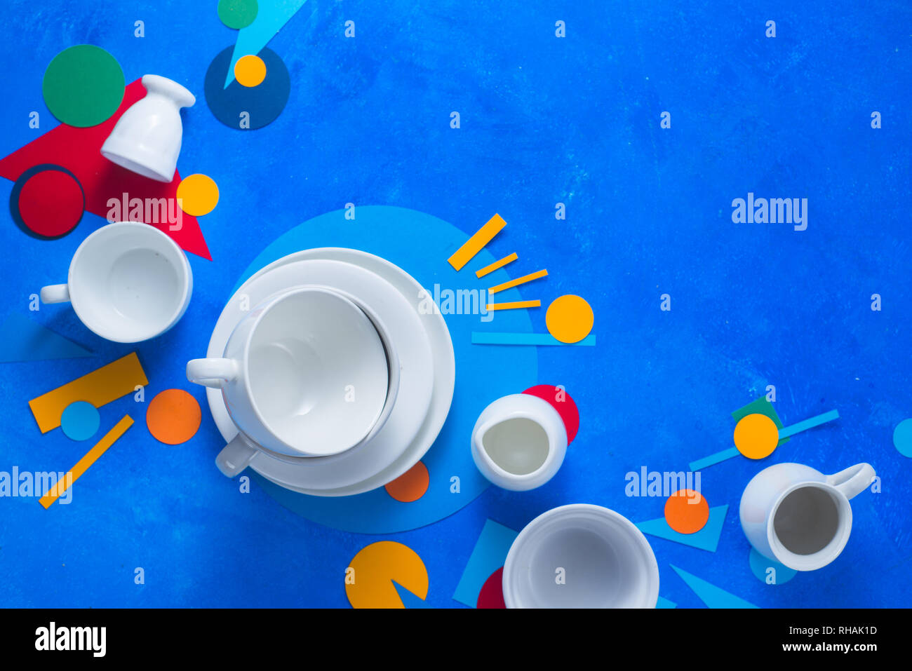 White piatti e tazze su uno sfondo colorato con forme geometriche. Blocco colore stoviglie laici piatta con copia spazio. Foto Stock