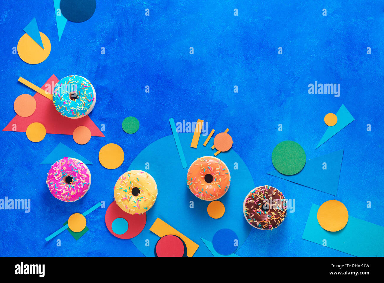 Le ciambelle con colorate decorazioni di carta. Il blocco di colore piatto intestazione laici con i dolci. Cucina creativa la fotografia con spazio di copia Foto Stock