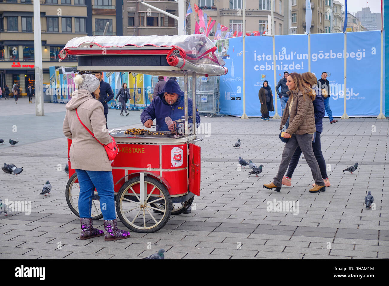Donna acquisto di castagno da un ambulanti carrello in una fredda giornata invernale. Sulla piazza Taksim, con curiosi. Istanbul, Turchia Foto Stock
