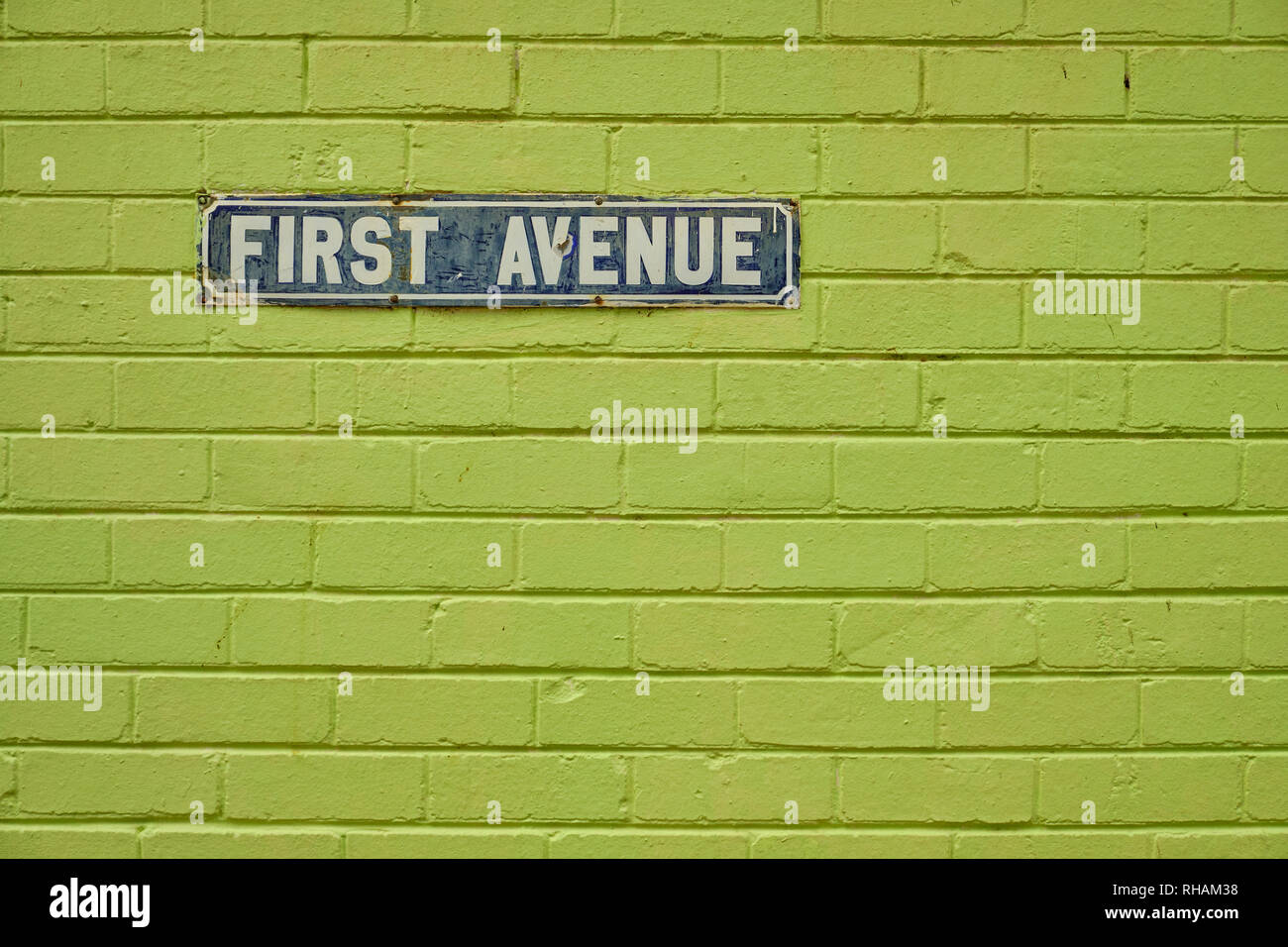 Vintage First Avenue strada segno, su un dipinto di verde un muro di mattoni. Segno è vecchio e mostra grande segno di usura e qualche ruggine Foto Stock