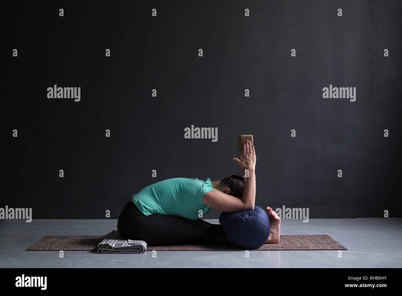 Donna pratica lo yoga, seduti piegare in avanti pone, mediante il blocco ed il piano di appoggio Foto Stock