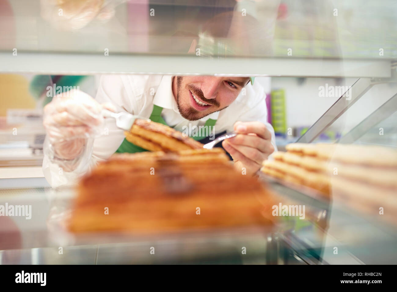 Giovane operaio in una pasticceria tenendo pezzo di torta per il cliente Foto Stock