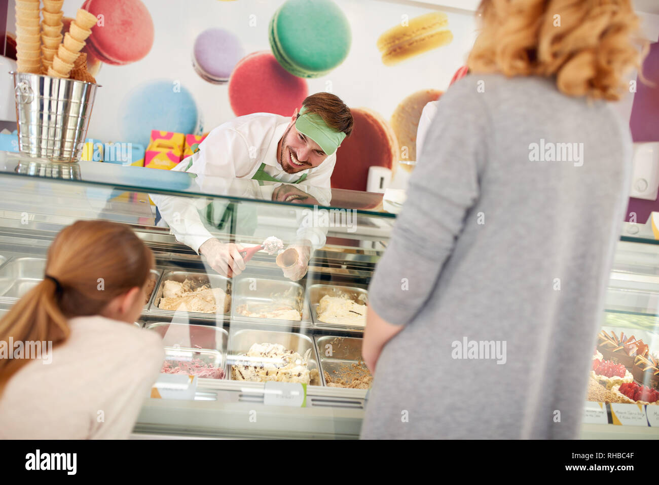 Sorridente negoziante maschio in pasticceria serve la ragazza con gelato Foto Stock