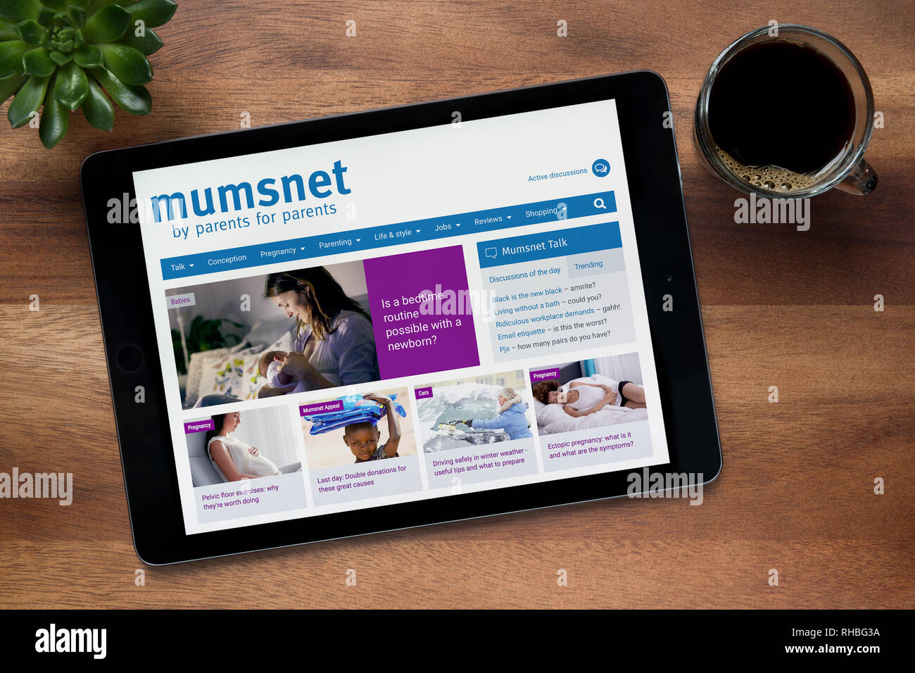 Il sito web di Mumsnet è visto su un tablet iPad, su di un tavolo di legno lungo con un caffè espresso e una pianta di casa (solo uso editoriale). Foto Stock
