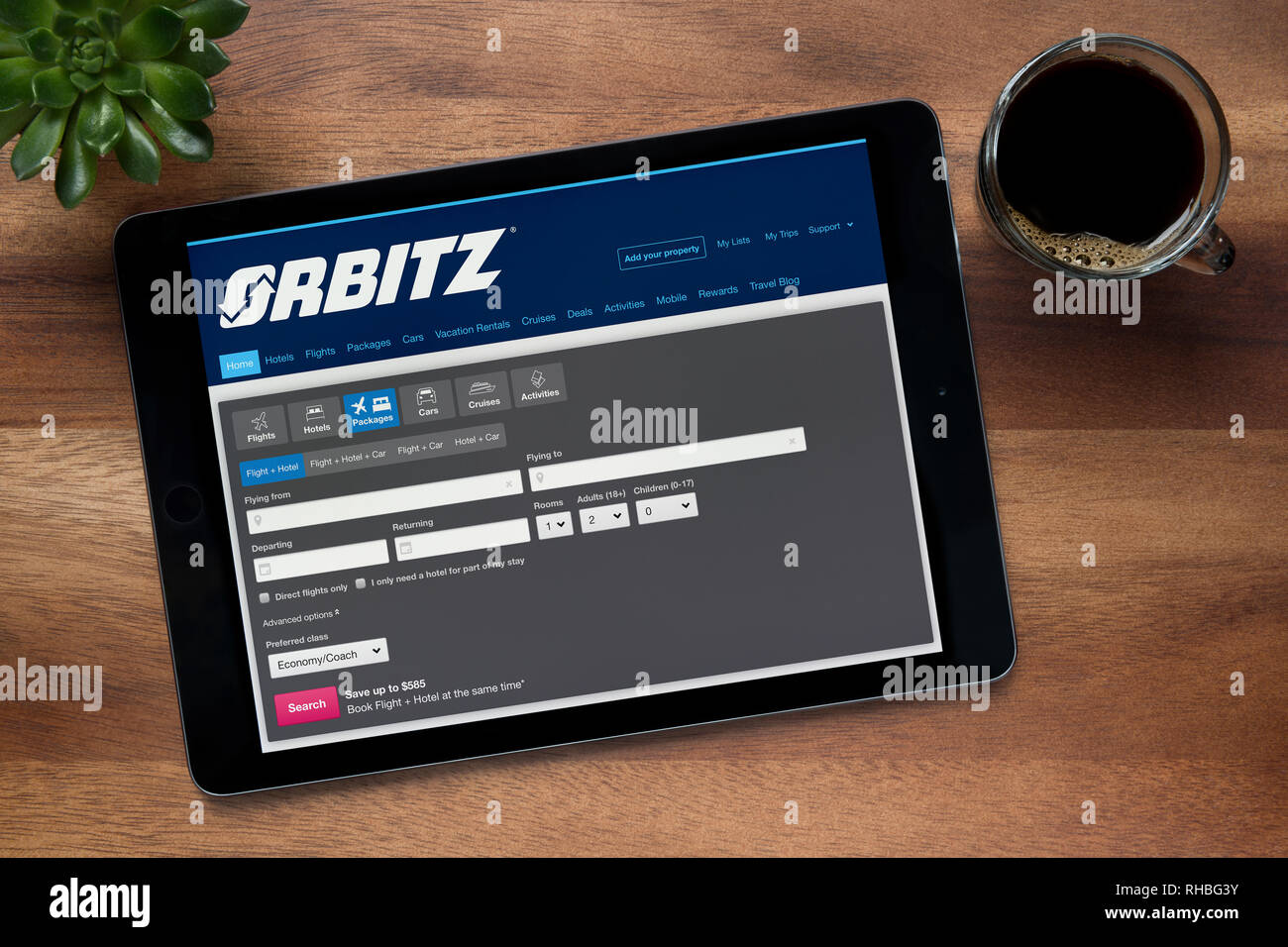 Il sito web della Orbitz è visto su un tablet iPad, su di un tavolo di legno lungo con un caffè espresso e una pianta di casa (solo uso editoriale). Foto Stock