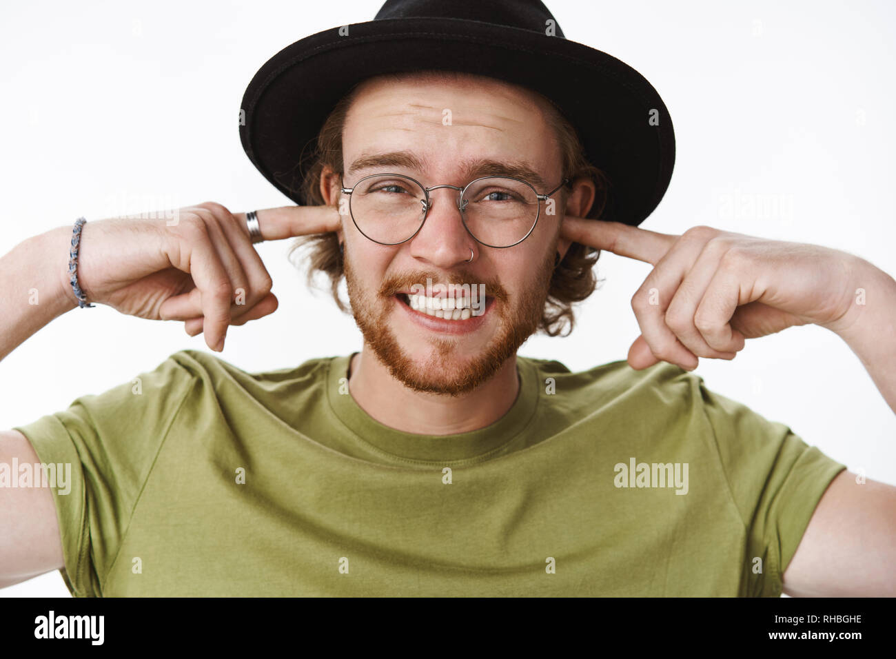 Si gioca davvero male. Ritratto di miserabili orinato giovane maschio muscian sente rumore terribile o music plug indice delle dita nelle orecchie stringere i denti e Foto Stock