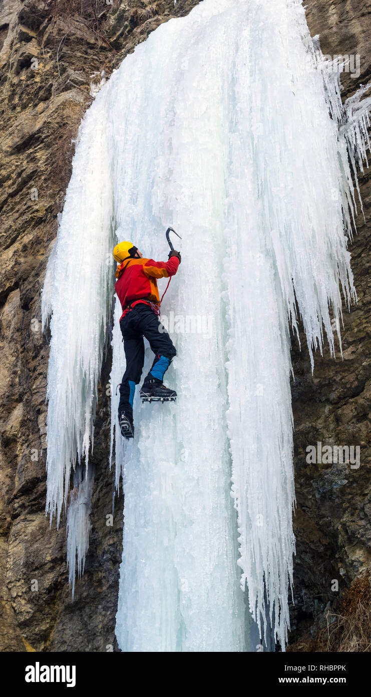 L'uomo la scalata di cascate ghiacciate con piccozze e ramponi. Extreme arrampicata su ghiaccio. Inverno Foto Stock