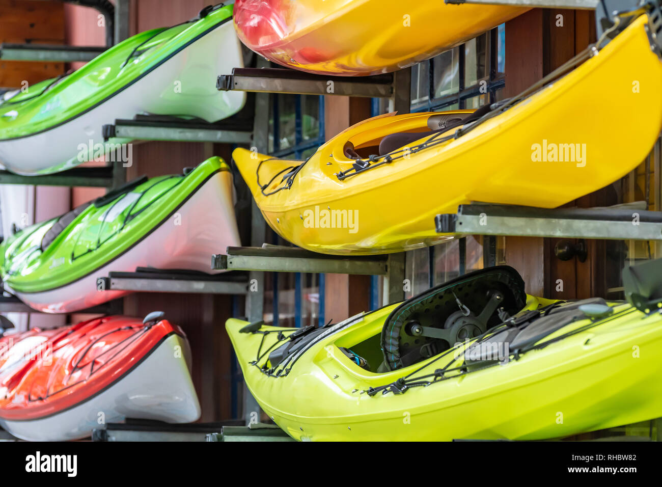 Colorate vivacemente colorato kayak noleggio impilati al di fuori di un negozio di sport acquatici Foto Stock