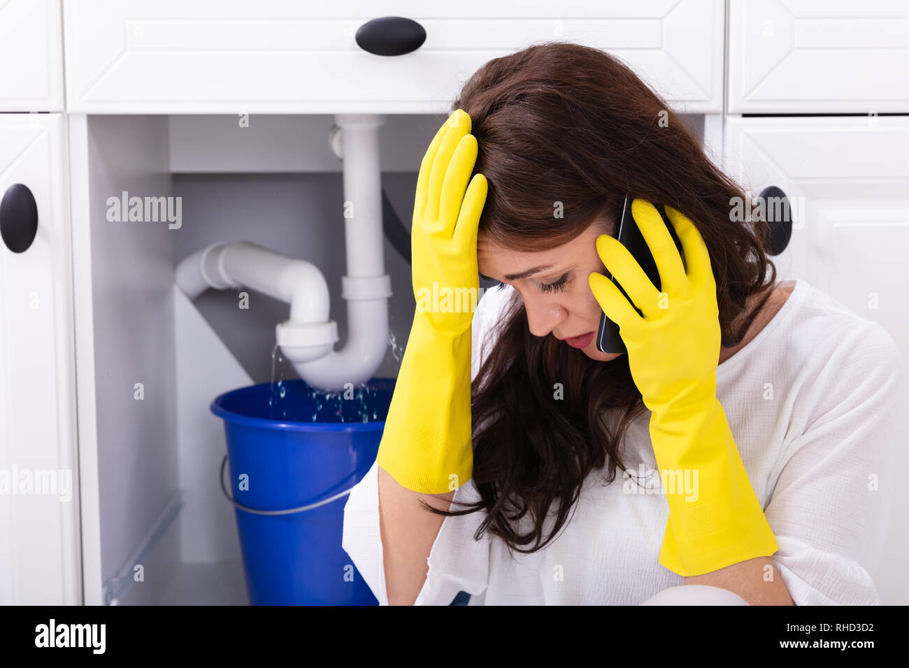 Triste giovane donna chiamando l'idraulico a fronte di perdite di acqua dal condotto del dissipatore Foto Stock