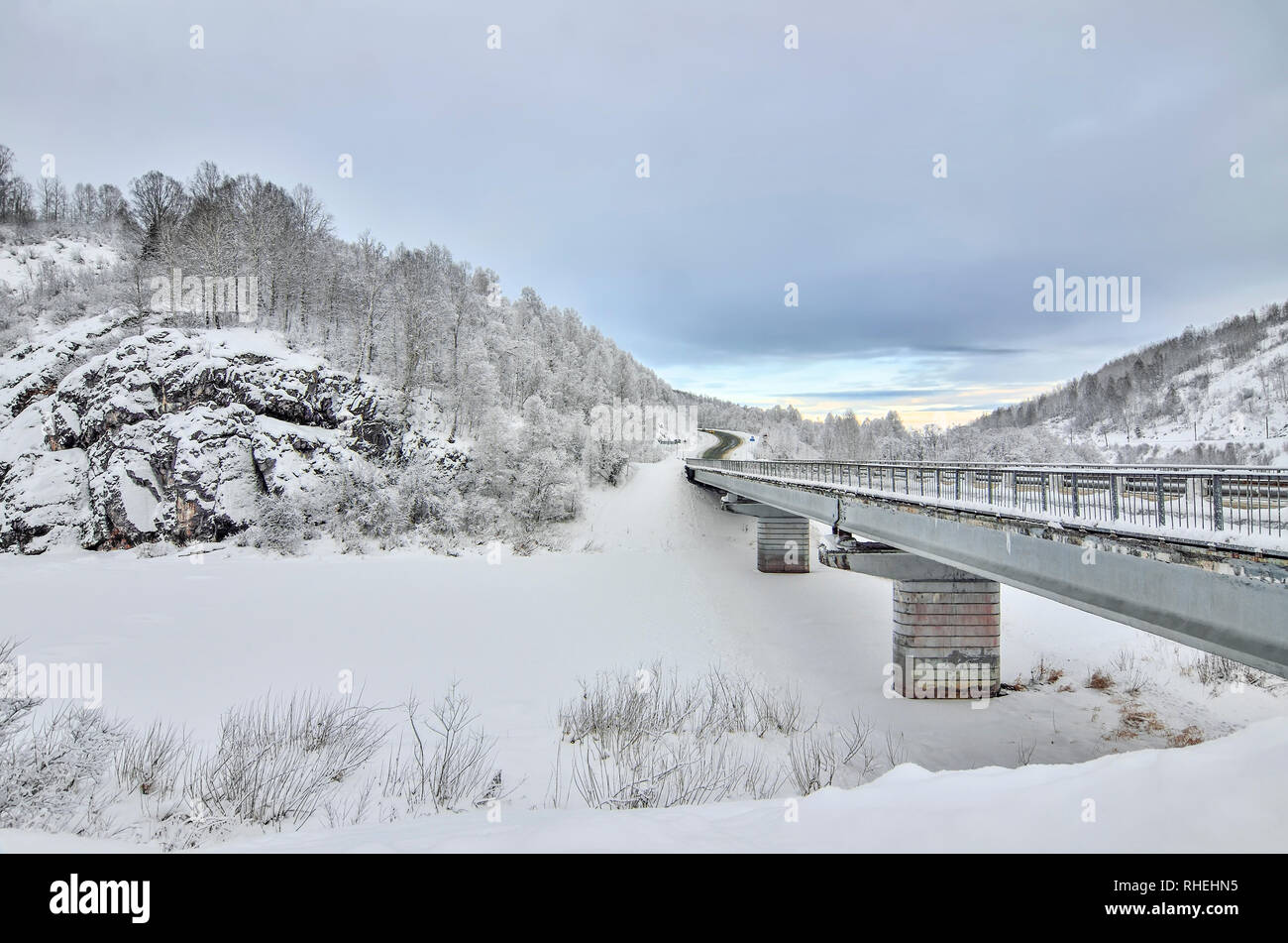 Autostrada con ponte attraverso le scogliere innevate in montagna - inverno bellissimo paesaggio al crepuscolo. La betulla e la foresta di pini sulle pendici delle colline con hoa Foto Stock