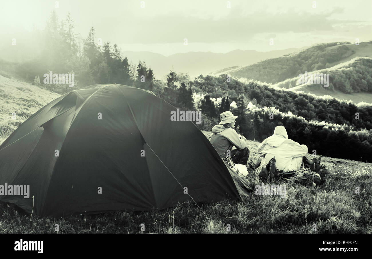 Bianco e nero Foto di viaggio. Due turisti seduti vicino a una tenda e guardando il paesaggio. Sole splende su una tenda. Effetto vintage. Rumore aggiunto Foto Stock