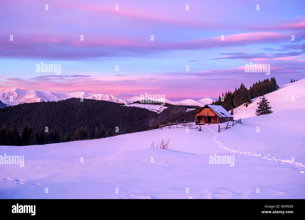 Romantico paesaggio di lonely capanna in legno nella luce rosa di Alba. Sullo sfondo montagna innevata cresta. Foto Stock