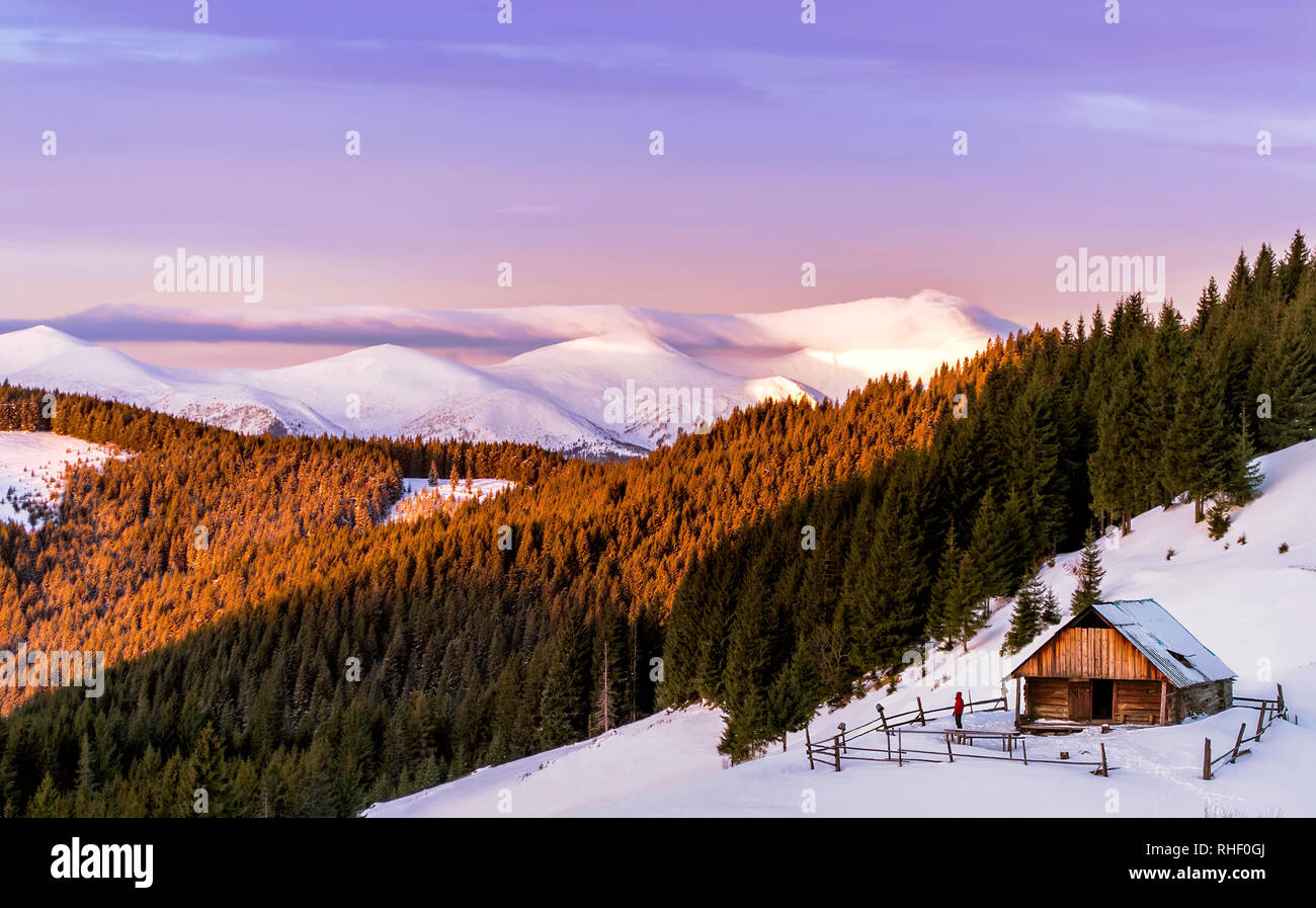 Cottage di legno sullo sfondo di un cielo rosa e montagne innevate al sole del mattino. Con gli uomini del cantiere. E la foresta di pini. Carpazi, Ukrain Foto Stock