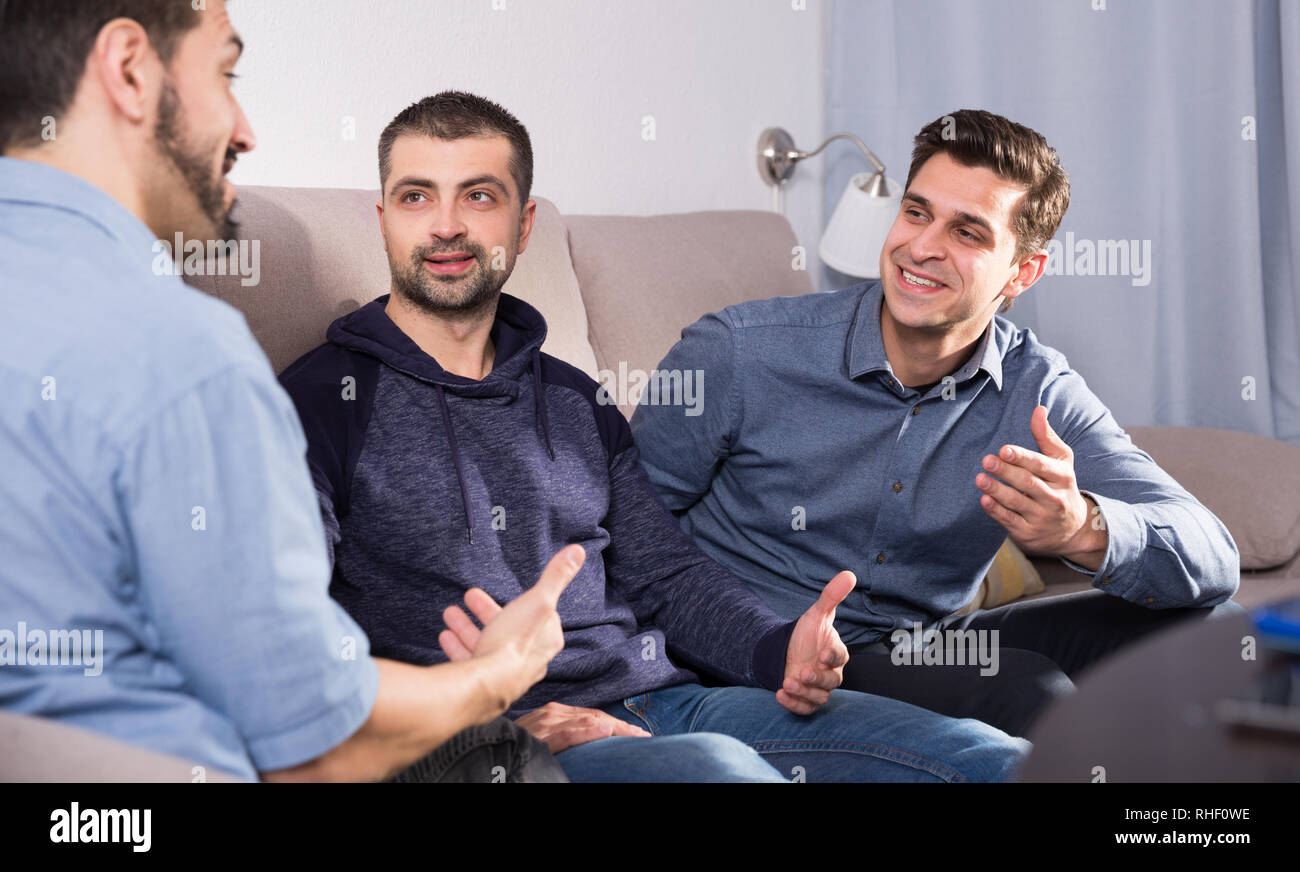 Tre amici maschi aventi divertente parlare comodamente seduti sul divano di  casa Foto stock - Alamy