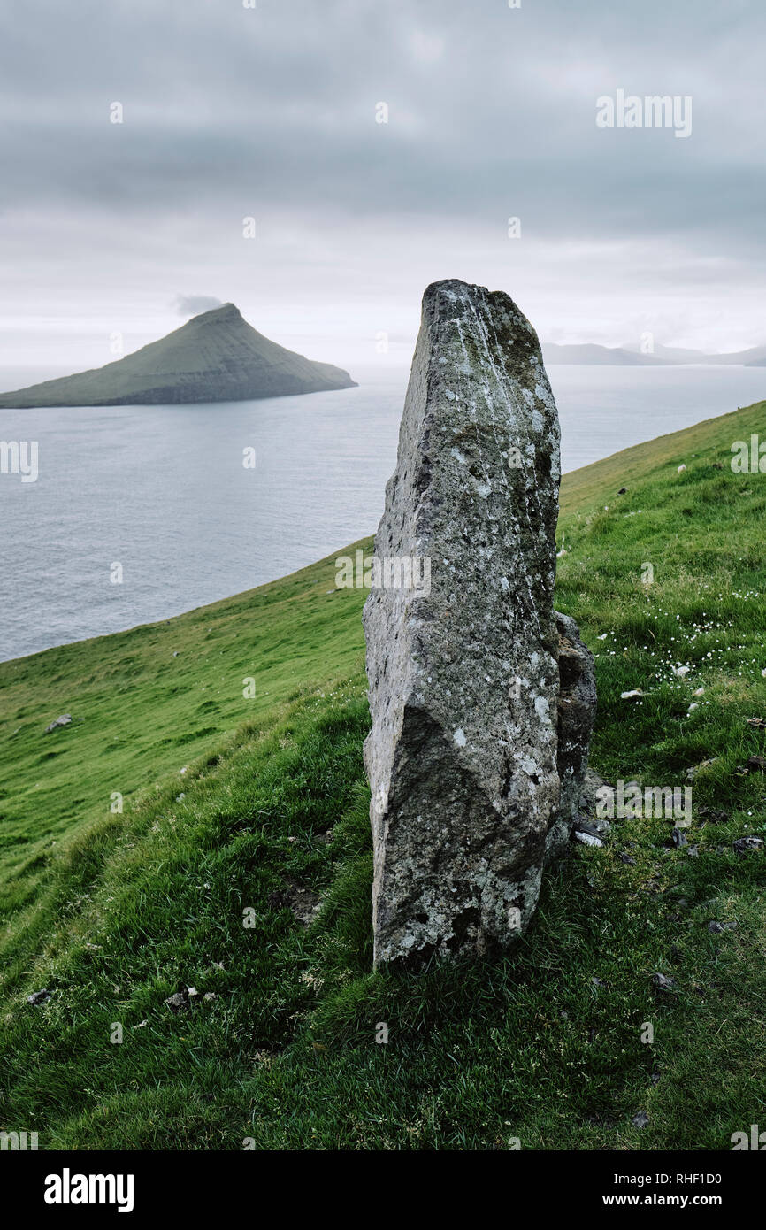 Un solitario pietra permanente su Streymoy affacciato Koltur isola nelle isole Faerøer. Foto Stock