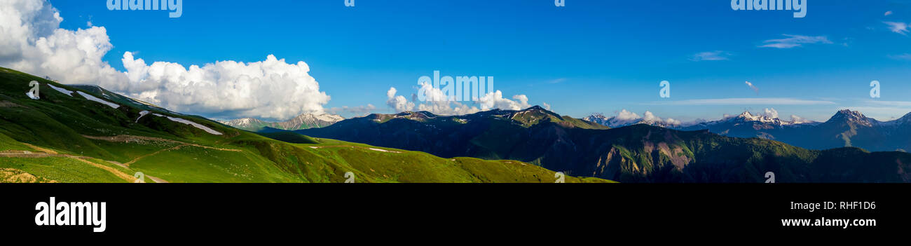 Ampio panorama di montagna.verdi colline con neve sui picchi di sera la luce del sole. Ombre scure. Blu cielo con alcune nuvole. Estate in Georgia. Foto Stock