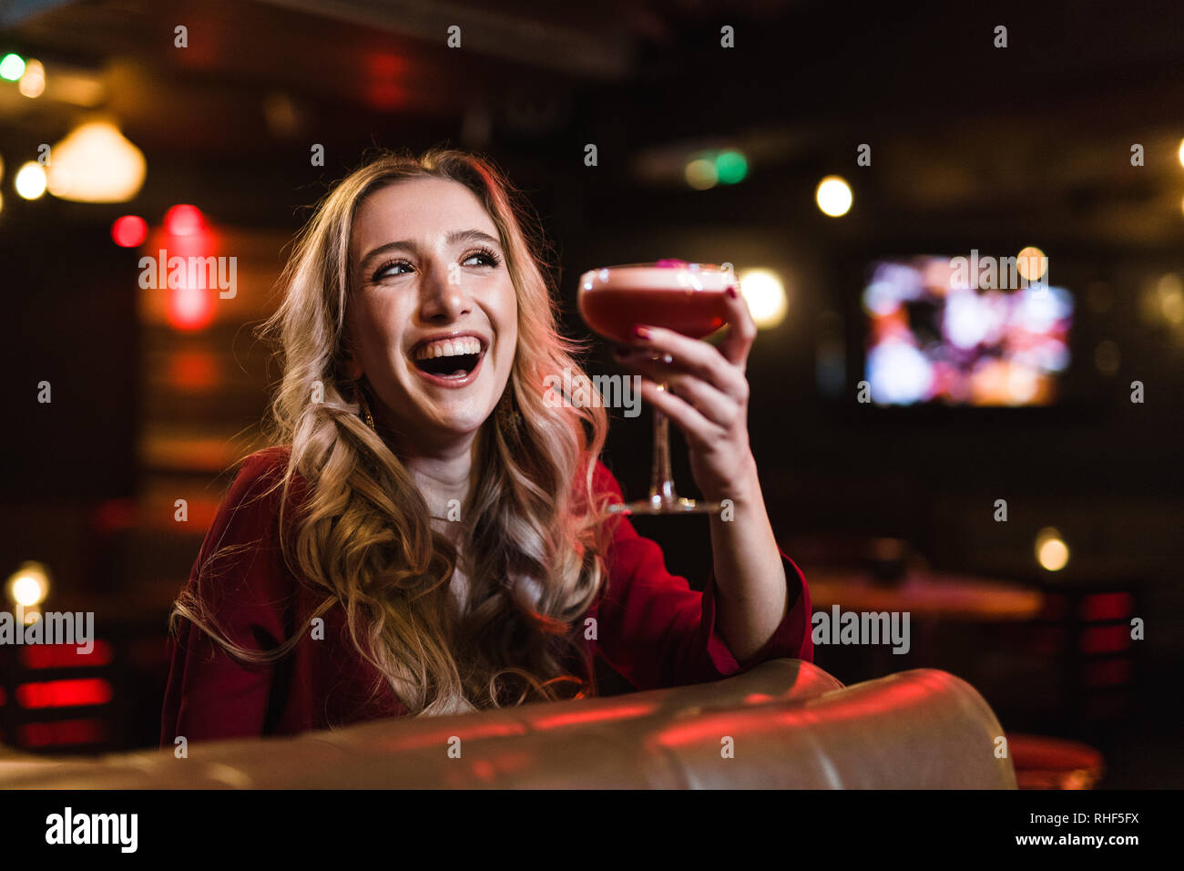 Un allegro giovane donna bionda in un bar, tenendo in mano un cocktail di rosa Foto Stock