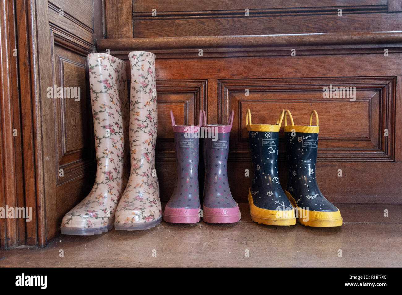 Tre paia di scarponi da Wellington - un adulto e due bambini - in un portico di una casa Foto Stock
