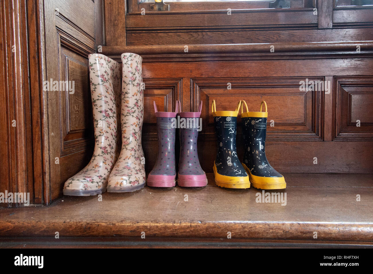Tre paia di scarponi da Wellington - un adulto e due bambini - in un portico di una casa Foto Stock