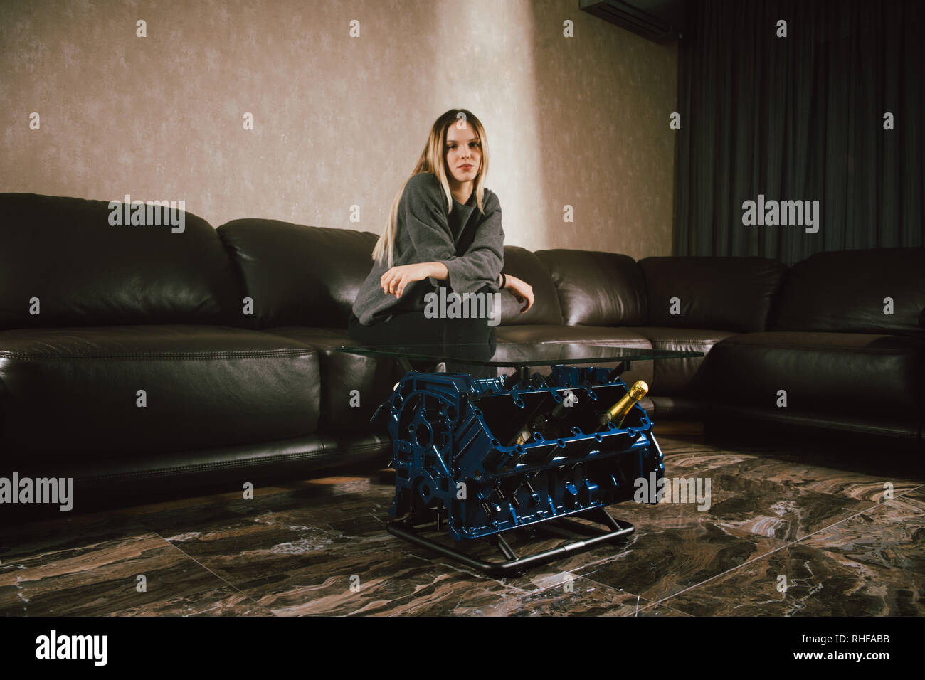 Giovani caucasici ragazza bionda seduta sul divano di interni di lusso personalizzato con la v8 motore auto tabella. Foto di moda e il bel sorriso Foto Stock