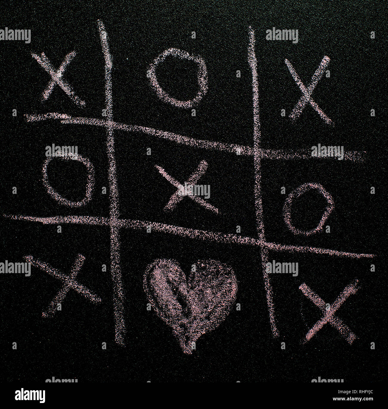 Tic-tac-toe gioco sul bordo nero. Il giorno di San Valentino concetto con tic tac toy simboli scritti con Chalk. XO XO simboli e forma di cuore. Foto Stock