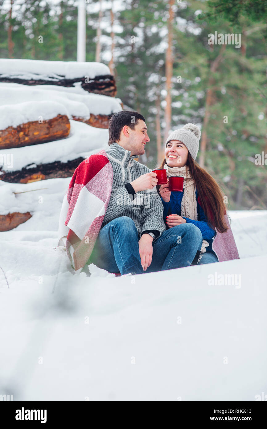 Sorridente giovane coppia con tazze di seduta in snow park. Bere bevande calde, divertendosi. Foto Stock