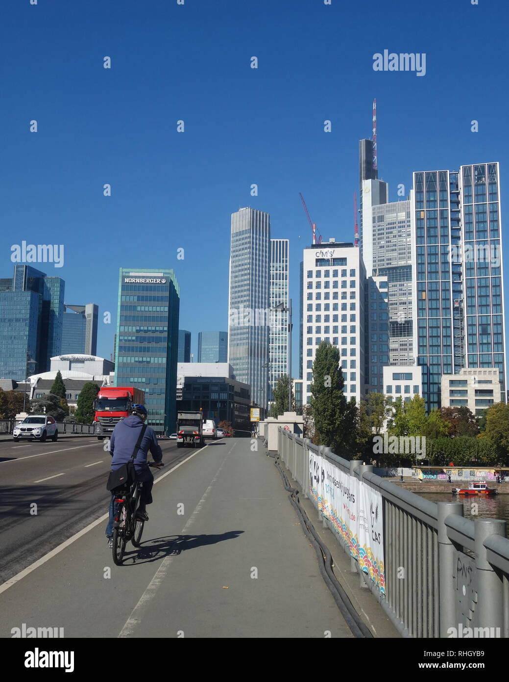 Un uomo di cicli attraverso il ponte Untermainbrücke verso l'skyscapers del quartiere finanziario in una limpida giornata di Francoforte nel 2018. Foto Stock