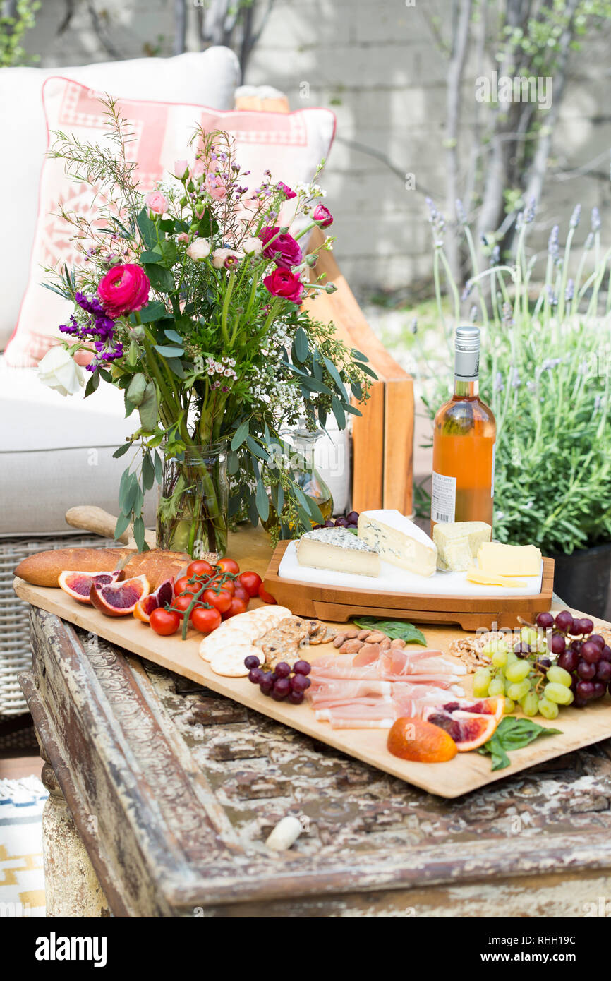 Scheda di formaggio con salumi e fiori sul cortile esterno partito picnic con vino e tavolo da caffè. Foto Stock