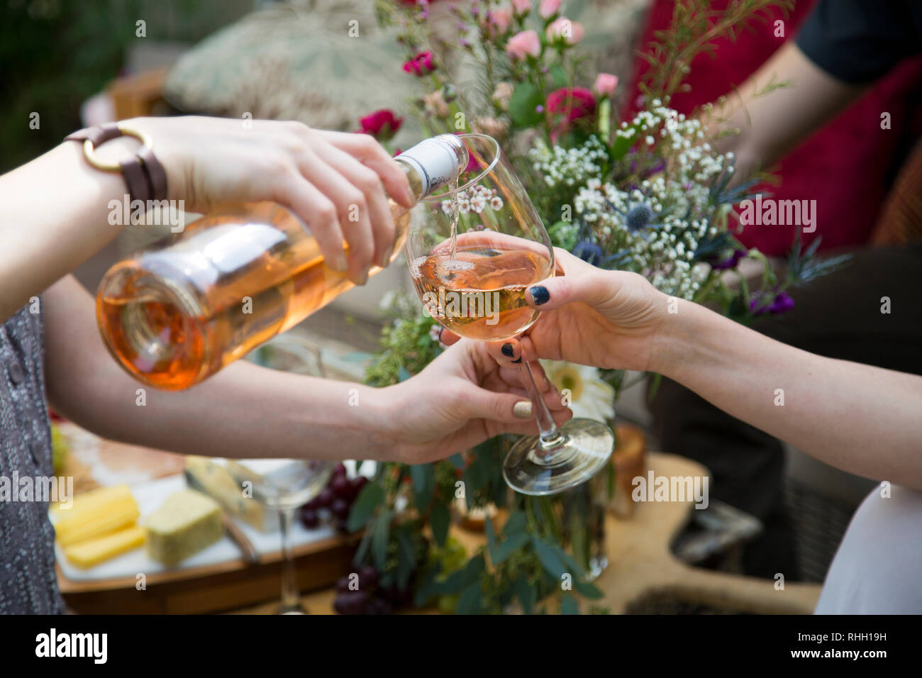 Mani amiche versare il bicchiere di vino rosato al partito del cortile con fiori. Foto Stock