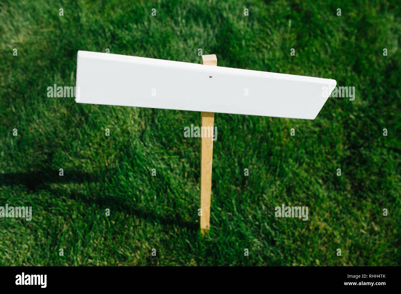 Breve erba tagliati con il bianco vuoto vuoto piccolo cartello in legno. Close up. Foto Stock