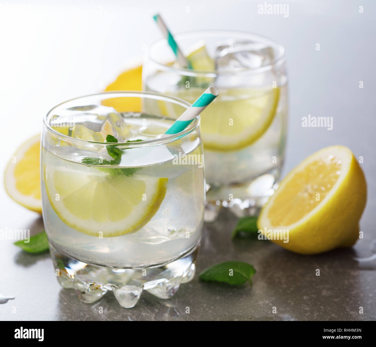 Due bicchieri di limonata con ghiaccio, menta e tagliare i limoni su uno sfondo grigio Foto Stock