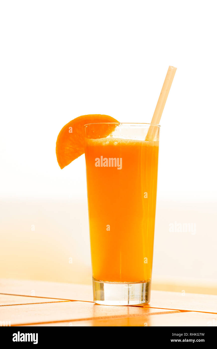Un bel bicchiere di succo d'arancia fresco decorate con una fetta di pane e una paglia su una tavola di legno Foto Stock