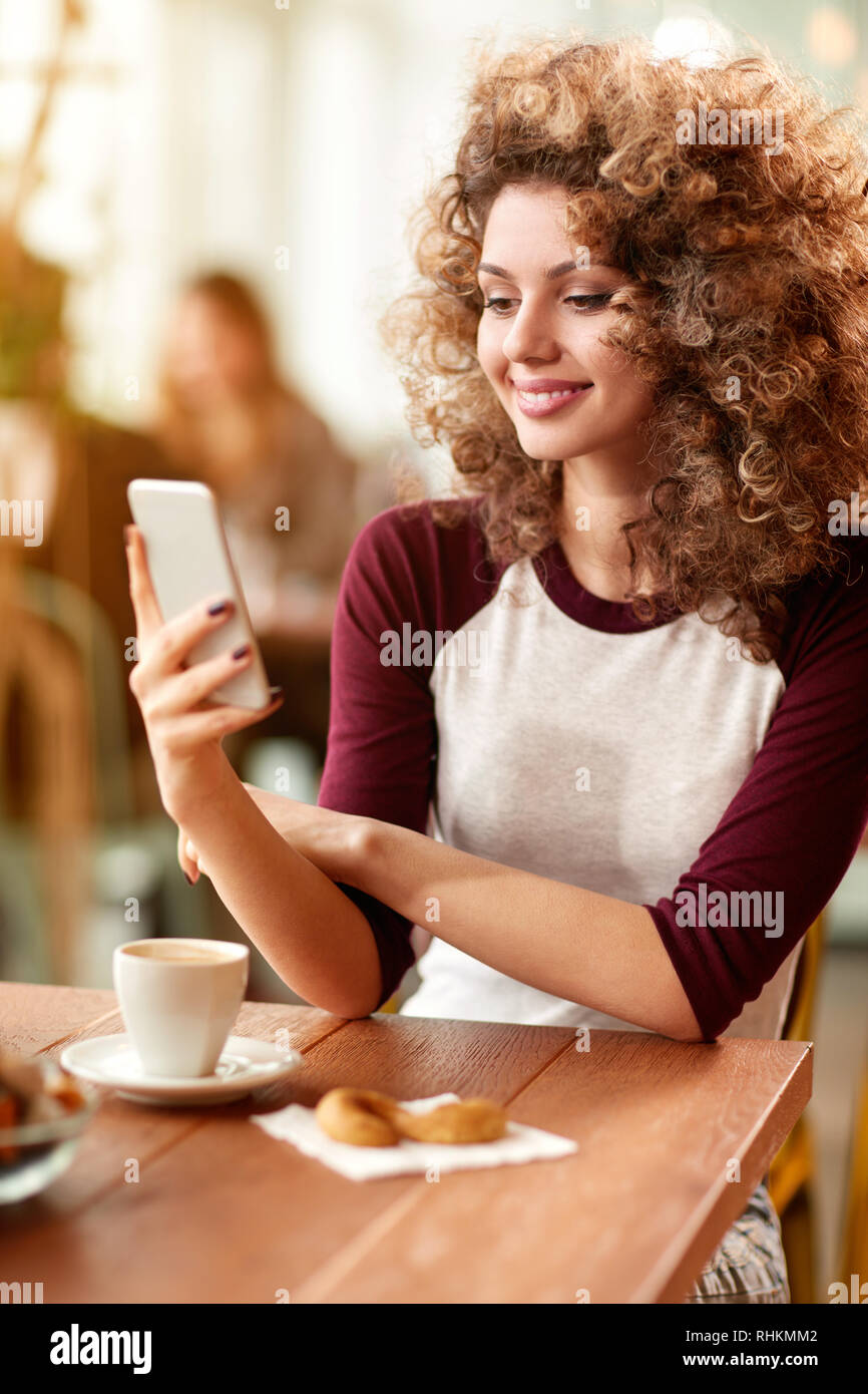 Curly giovane donna con il cellulare in ristorante Foto Stock