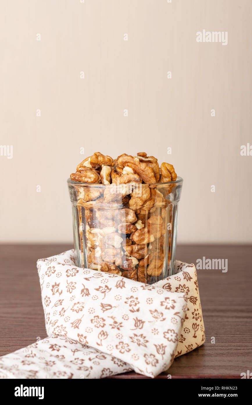 Fresche le noci sbucciate in un bicchiere su un tavolo di legno con un bianco tovaglia fiorito, e lo spazio negativo per copiare il testo Foto Stock