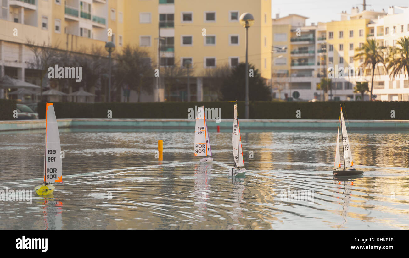 Piccola Vela barche giocattolo di gara. Mini remote di Stagno controllato le barche a vela e yacht in una piccola città sul lago al tramonto con bella luce dorata, golden hou Foto Stock