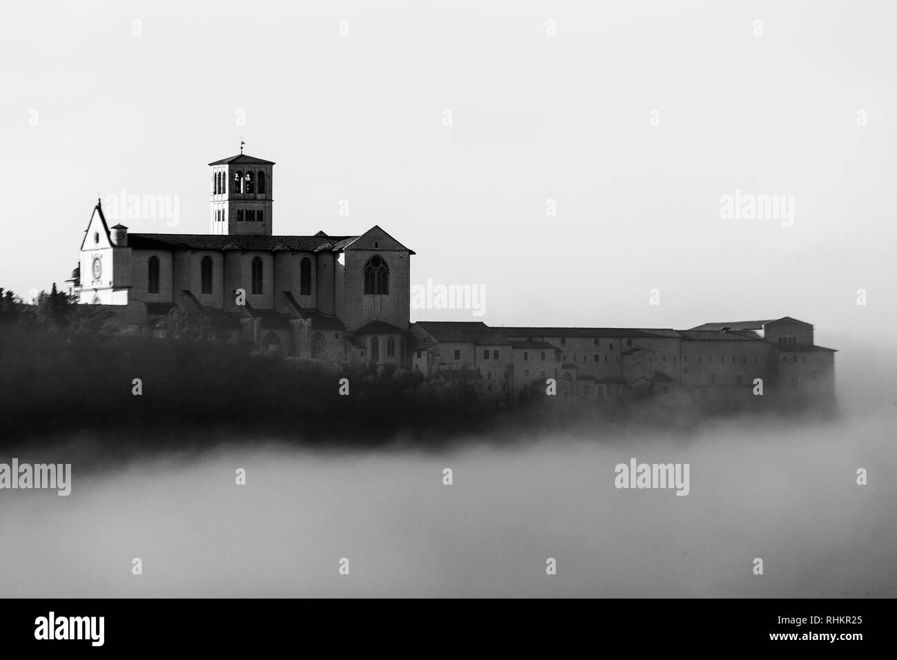 Una vista della Basilica di San Francesco in Assisi nel mezzo della nebbia sotto un cielo profondo con le nuvole Foto Stock