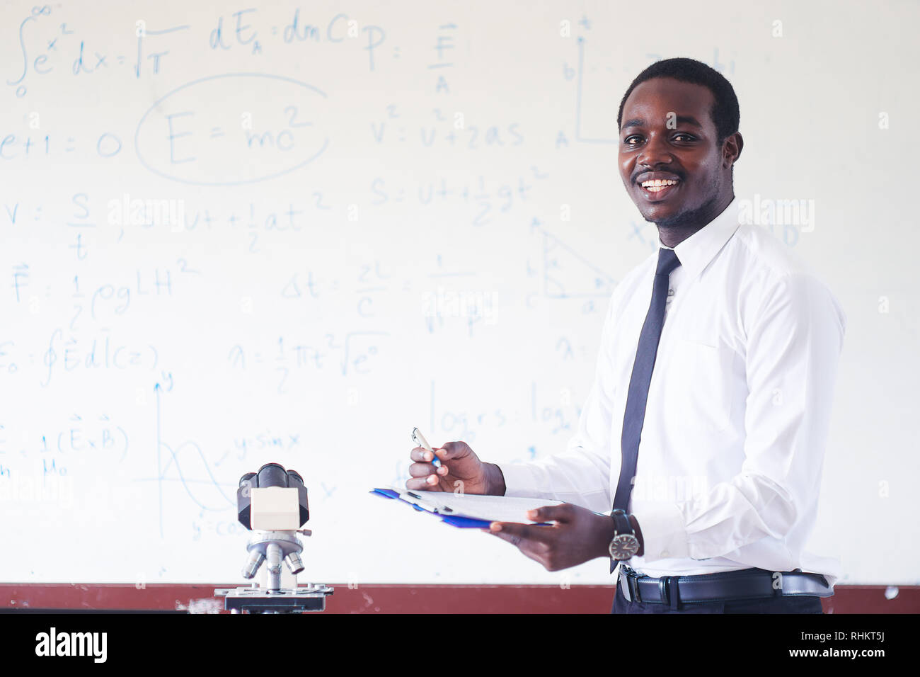 African insegnante di scienze insegnamento e sorridente nel gambo di classe con microscopio. Foto Stock