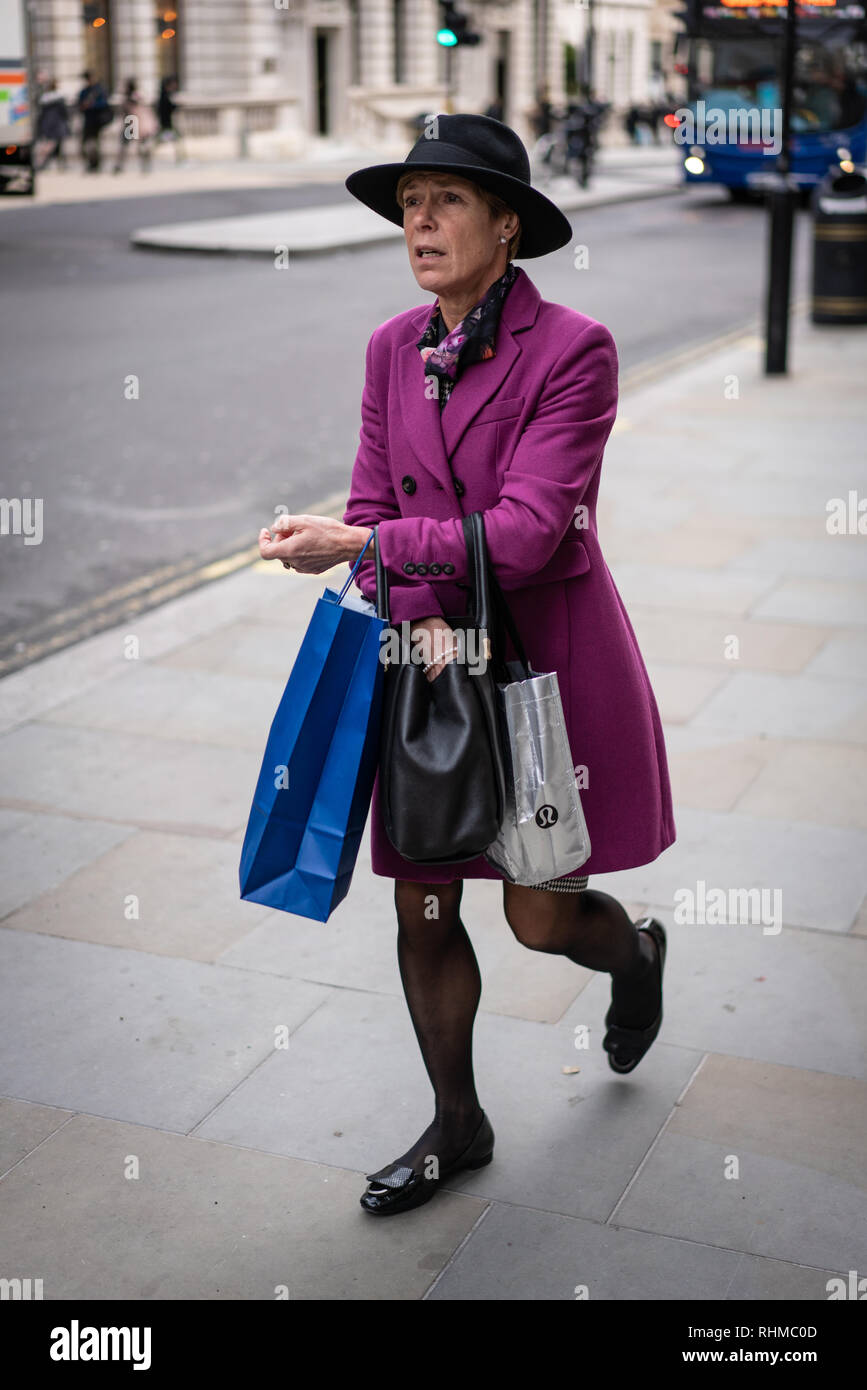 Ben vestito business lady indossando un cappello si fa strada lungo una trafficata strada di Londra in inverno, REGNO UNITO Foto Stock