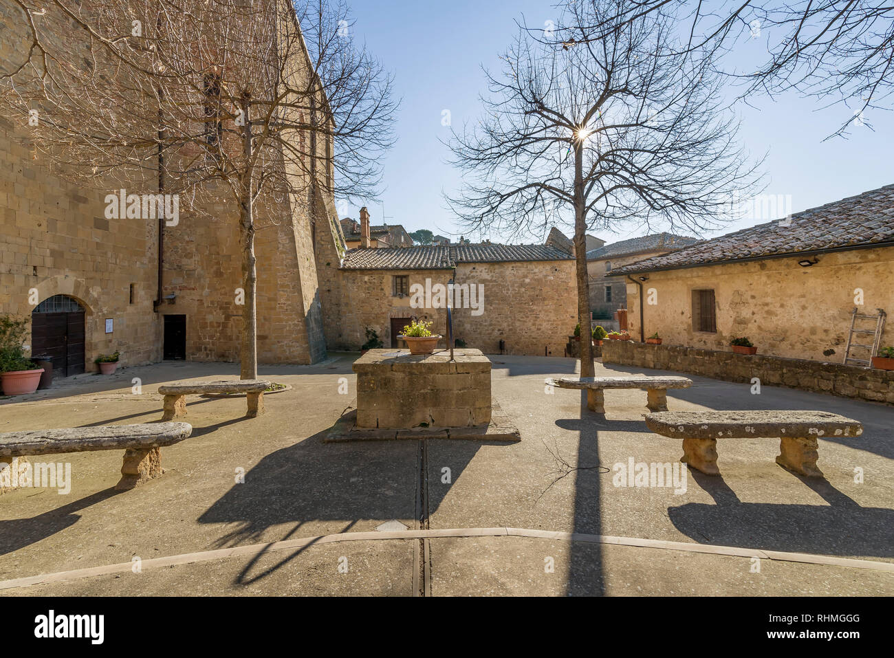 Il sole filtra attraverso i rami di alberi in Piazza Commenda di Monticchiello, Siena, Toscana, Italia Foto Stock