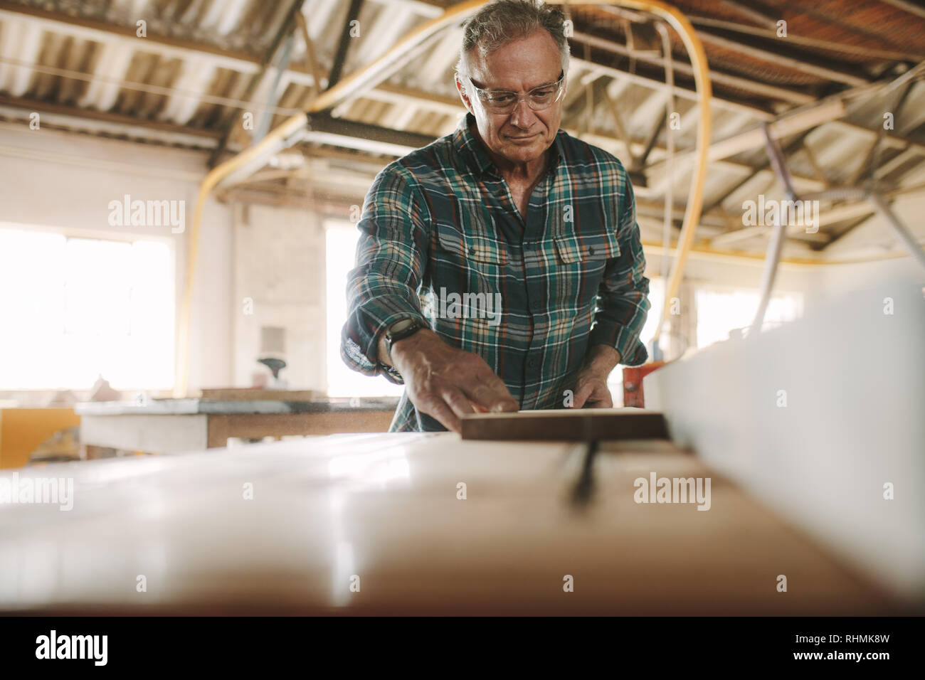 Senior falegname maschio lavora sul tavolo macchina sezionatrice. Uomo Taglio di listelli di legno sul tavolo macchina sezionatrice in falegnameria officina. Foto Stock
