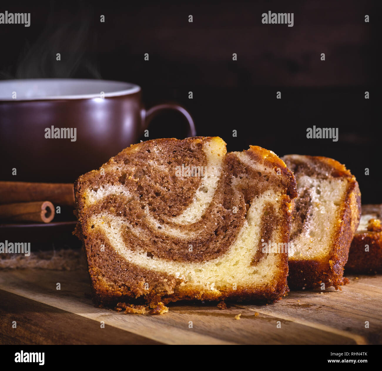 Primo piano di fettine di cannella swirl pane dolce e una tazza di caffè fumante contro un oscuro sfondo di legno Foto Stock