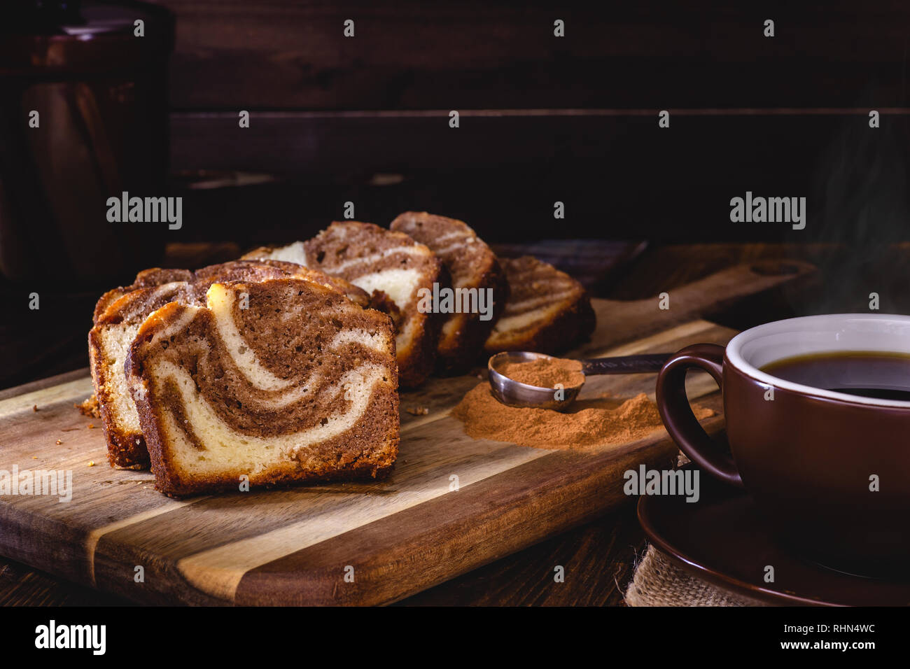 Fette di cannella swirl pane dolce con cannella spice su una tavola di legno e una tazza di caffè fumante contro un oscuro sfondo di legno Foto Stock