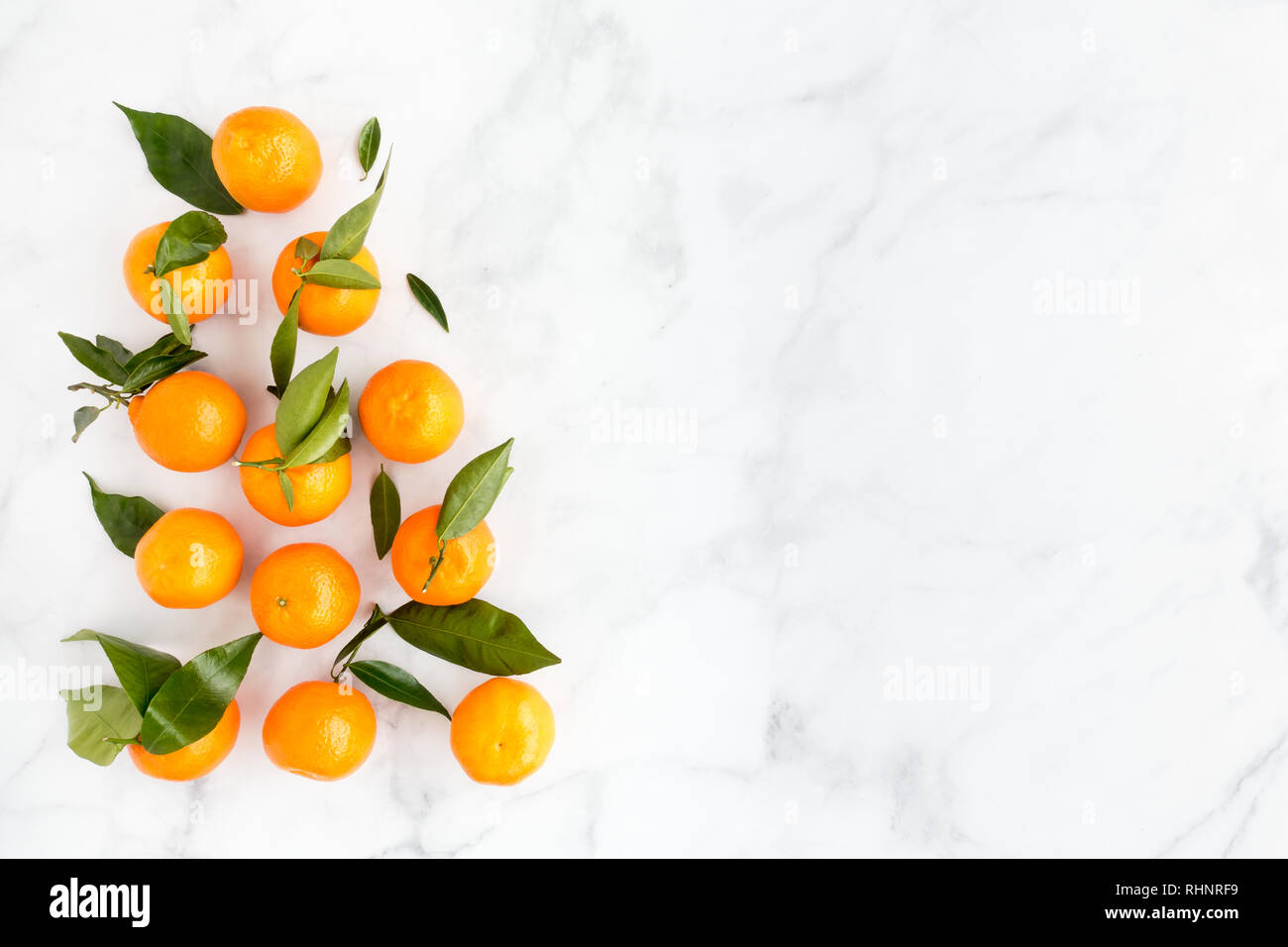 La disposizione delle clementine con foglie su marmo bianco lo sfondo con un sacco di spazio copia. Vista dall'alto. Foto Stock
