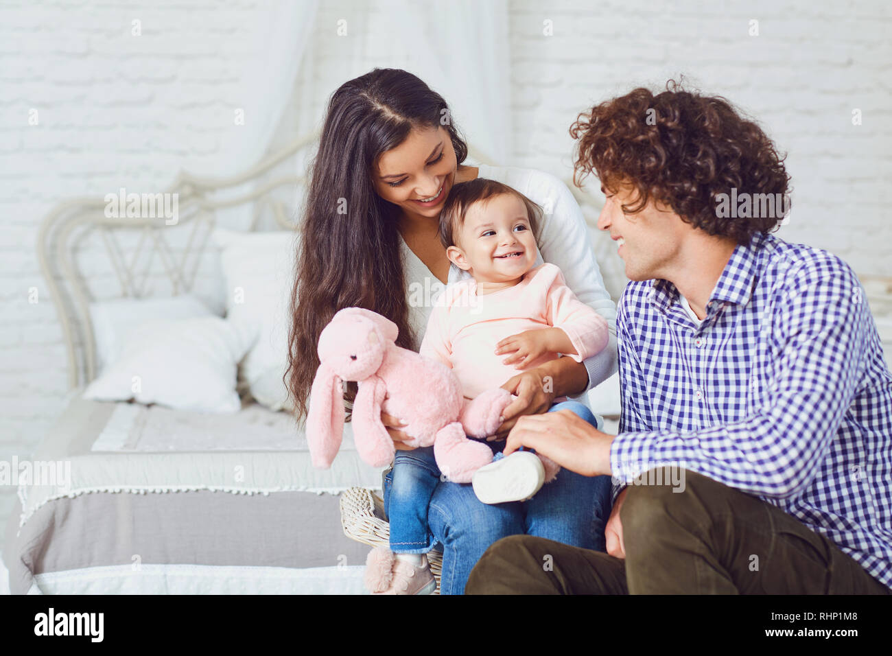 La famiglia felice giocando con il bambino in camera. Giovane madre e padre gioca con la figlia su un letto in ambienti chiusi. Foto Stock