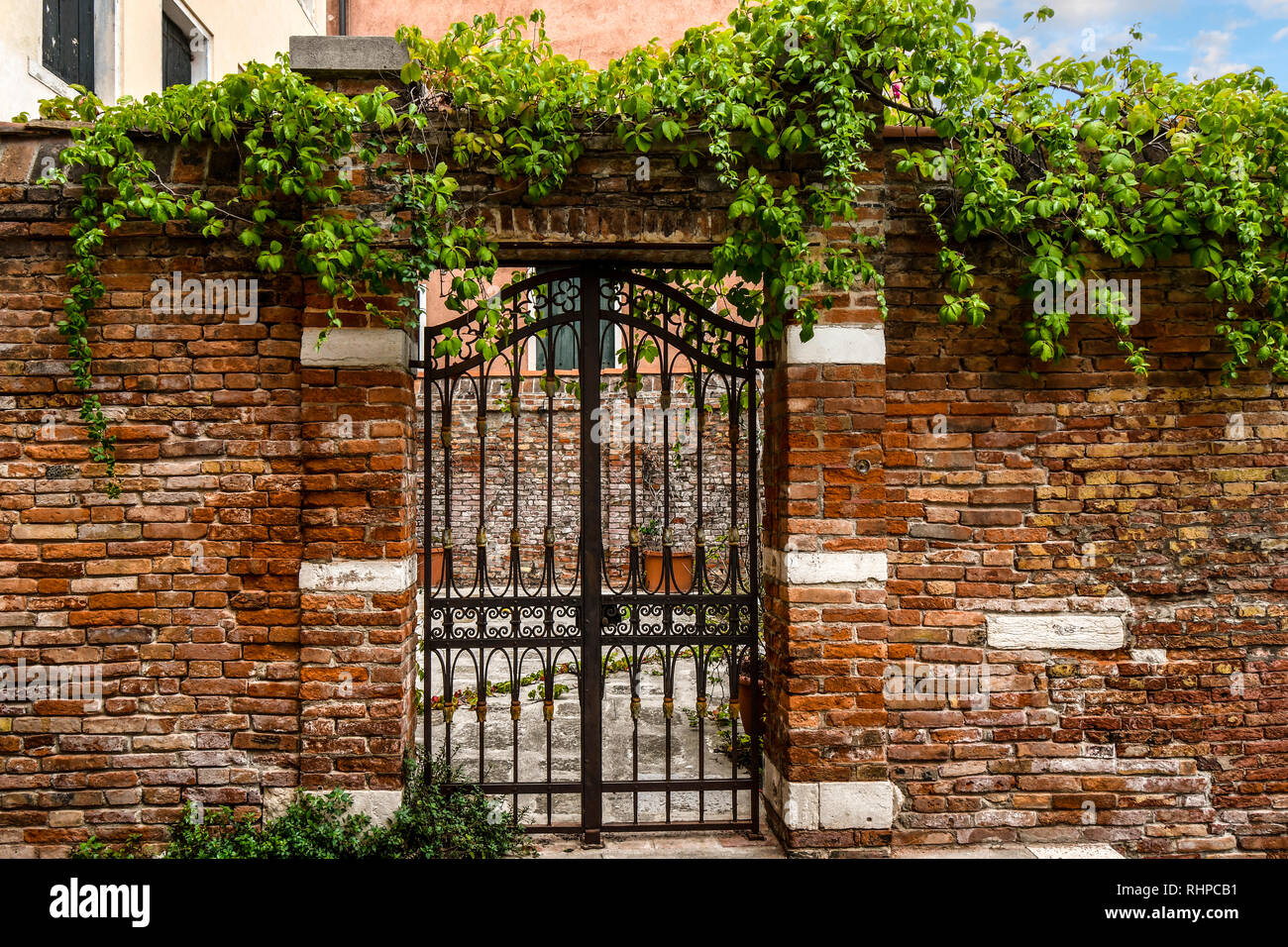 Una cancellata in ferro battuto e un muro di mattoni nella parte anteriore di un cortile medievale nel centro storico di Venezia, Italia Foto Stock