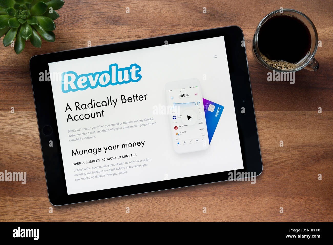 Il sito web di Revolut è visto su un tablet iPad, su di un tavolo di legno lungo con un caffè espresso e una pianta di casa (solo uso editoriale). Foto Stock