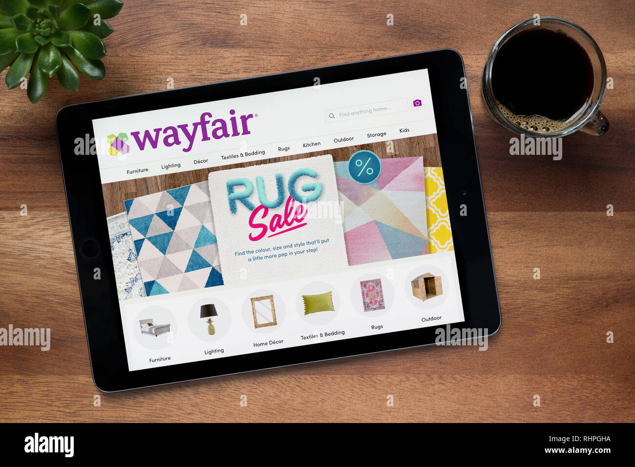 Il sito web di Wayfair è visto su un tablet iPad, su di un tavolo di legno lungo con un caffè espresso e una pianta di casa (solo uso editoriale). Foto Stock