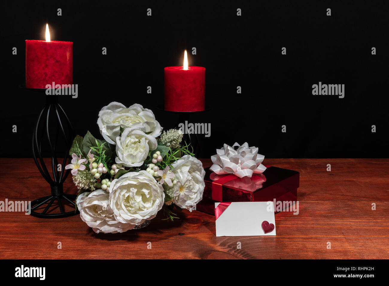 Bouquet di fiori disposti candele rosse su un supporto con un presente e una scheda su un tavolo di legno. Festa della mamma, Pasqua, valentines, compleanno, Foto Stock